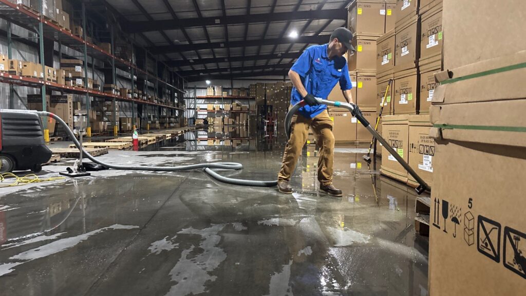 Restoration Pros technician using commercial water extractor to remove standing water in warehouse
